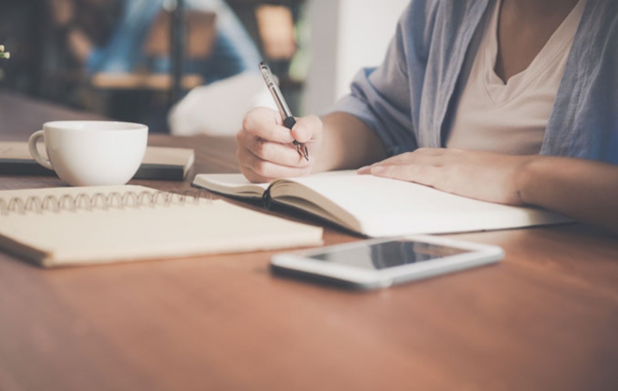 A person makes notes in a journal while sitting at a desk. 